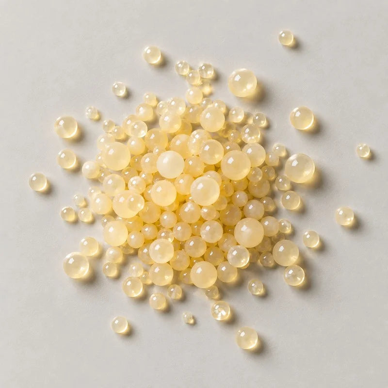 A scatter of pale yellow spherical retinol capsules in mixed sizes on a stone grey background
