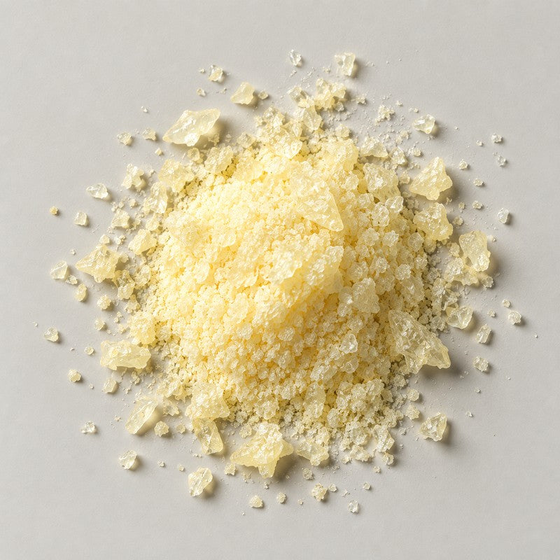A mound of pale yellow crystalline powder with coarse translucent shards scattered around it, on a stone grey background