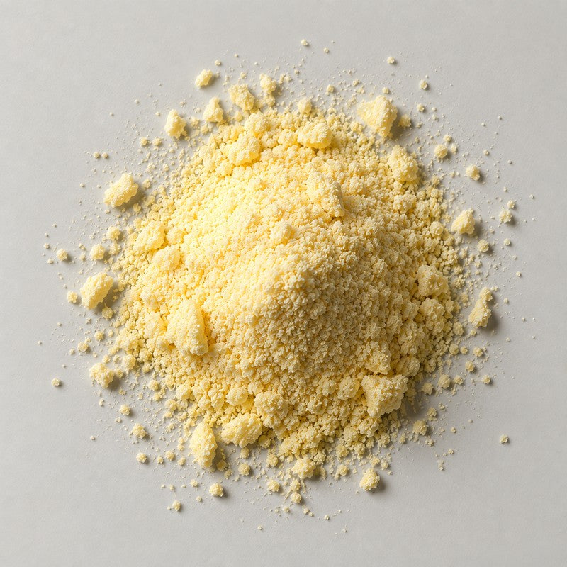 A mound of pale yellow crumbly powder with loose grains scattered around it, on a stone grey background